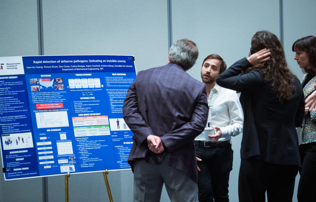 A man, standing by a scientific poster, speaks with another man and two women.