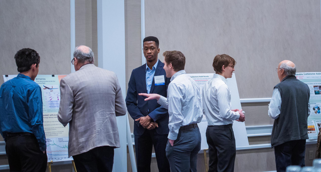 Six men look at scientific project posters.