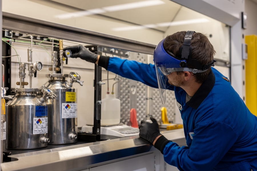 A man wearing protective clothing tweaks a laboratory device